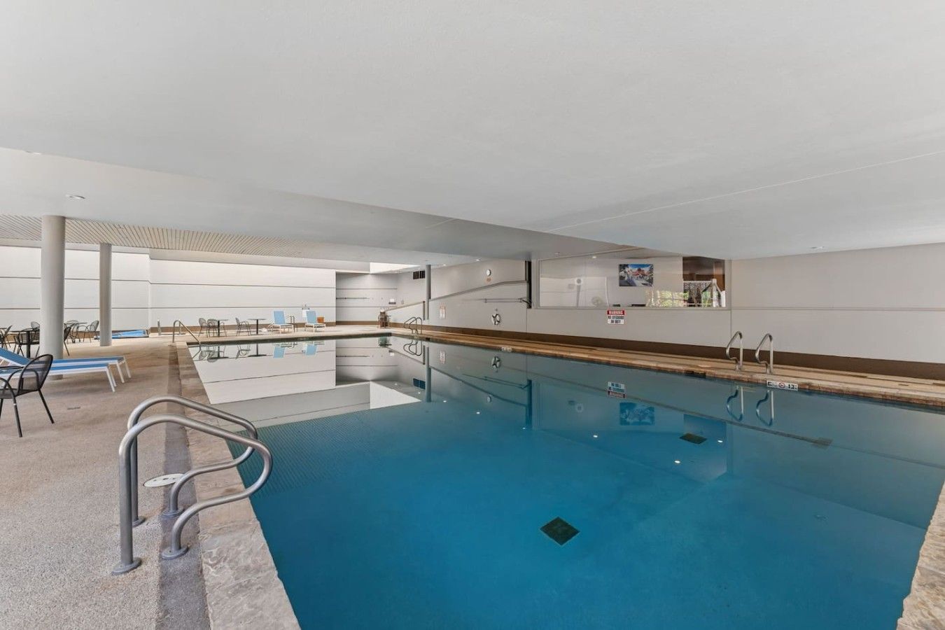 Una piscina interior con agua cristalina, un trampolín y sillas de descanso.