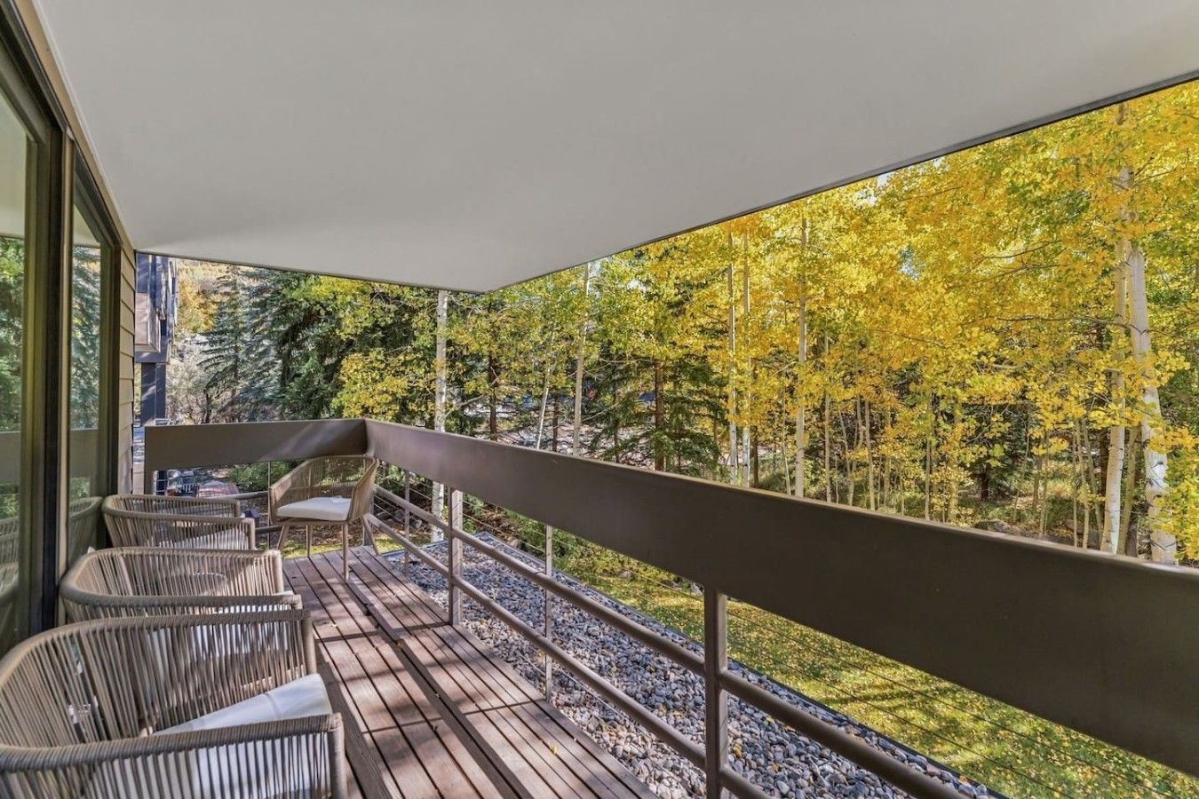 Un balcon agrémenté de meubles en osier et offrant une vue sur les arbres aux couleurs automnales.