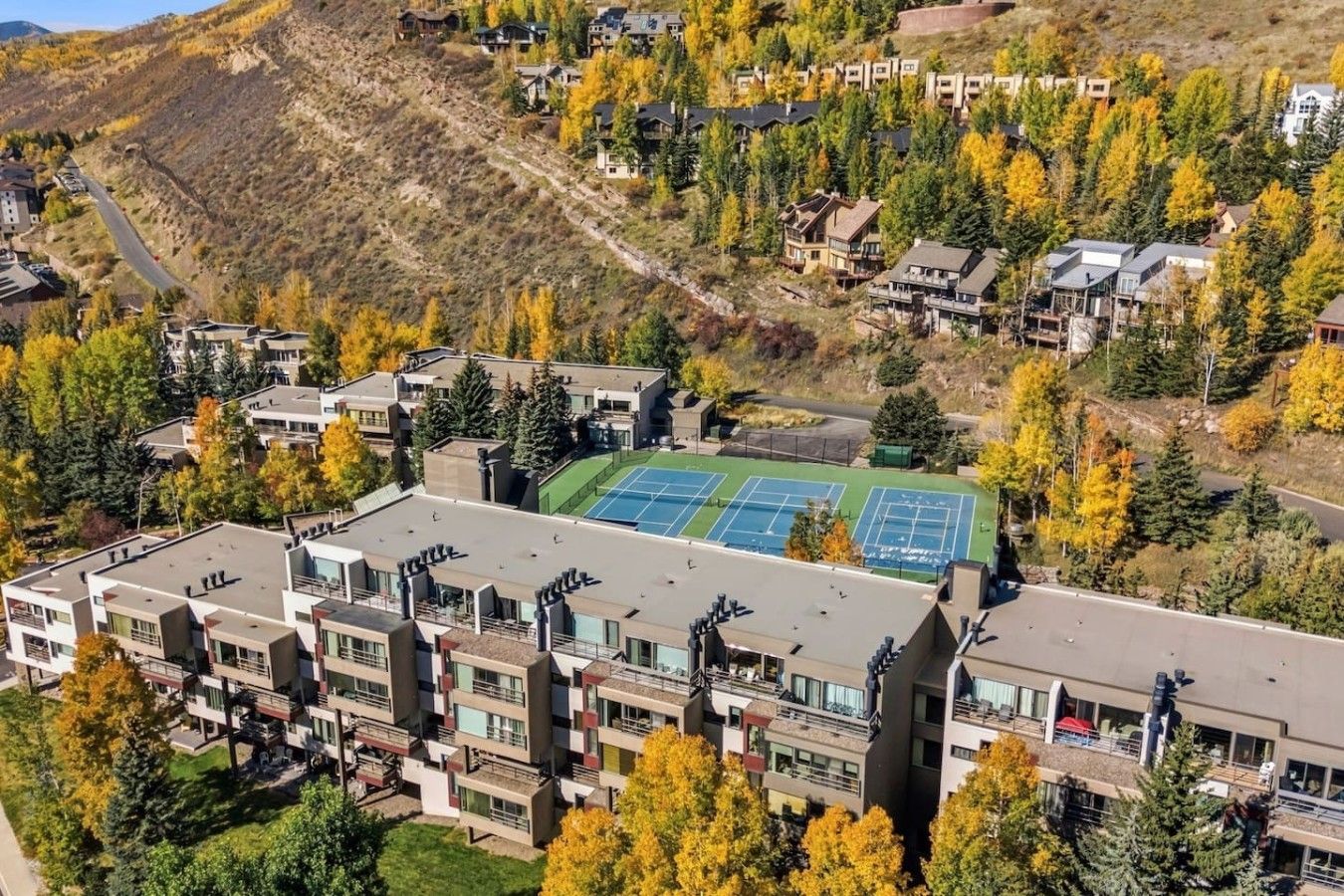 Zona residencial con edificios modernos, cancha de tenis y montañas al fondo.