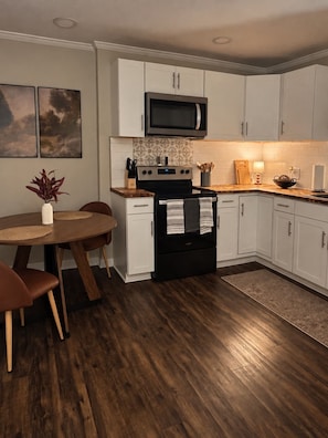Une cuisine moderne avec des meubles blancs, une cuisinière noire et un four à micro-ondes. On y trouve une table à manger avec des chaises et une plante accrochée au mur.