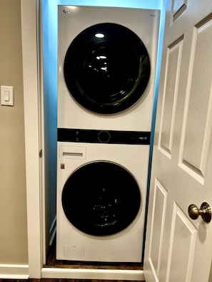 Un appareil compact, comprenant une laveuse et une sécheuse, conçu pour être fixé au mur, doté d’un panneau de commande et d’une étiquette de sécurité.