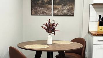 Un comedor con una mesa redonda, dos sillas, un florero con planta y dos cuadros en la pared.