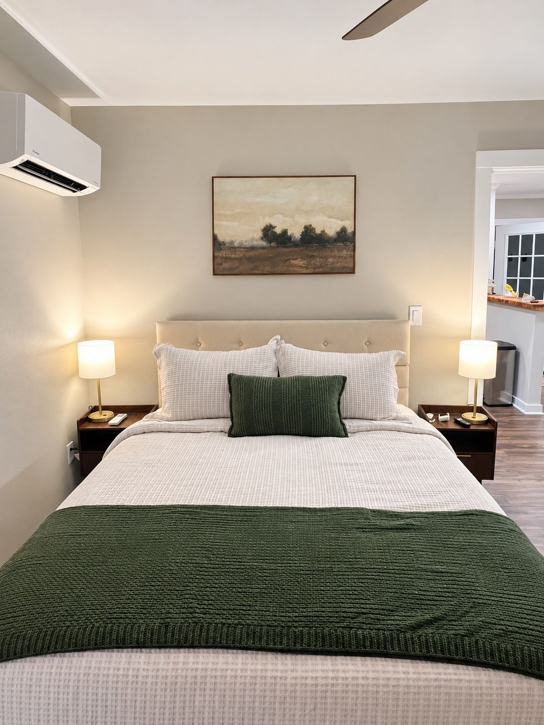 Ein Schlafzimmer mit einem Bett, zwei Nachttischen, einer Wand-Klimaanlage und einem Gemälde.
