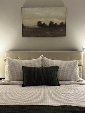 Une chambre à coucher avec un lit, des oreillers, une tête de lit et un tableau accroché au mur.