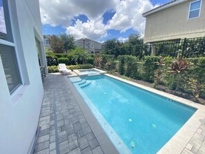 A rectangular swimming pool with a tiled deck, surrounded by greenery and a fence. - Elegant 8BR Family Home w/ Pool & Spa (Kissimmee)