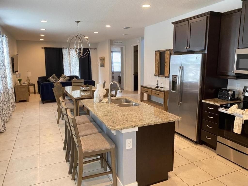 A modern kitchen with a central island, dark cabinetry, stainless steel appliances, and a dining area with a bar stool.