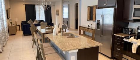 A modern kitchen with a central island, dark cabinetry, stainless steel appliances, and a dining area with a bar stool.