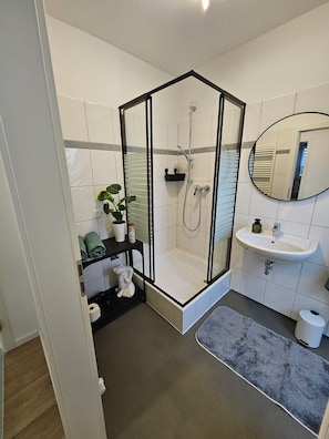 Un baño moderno con ducha de vidrio, lavamanos y espejo.