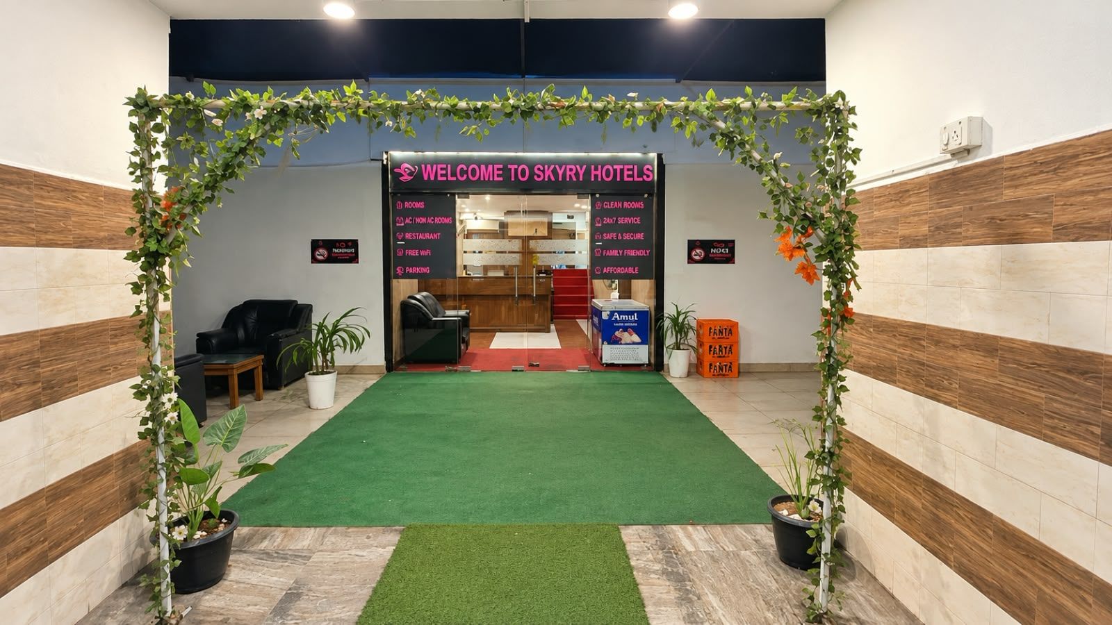 A reception area with a green carpet, reception desk, and a sign listing amenities like rooms, WiFi, and parking.