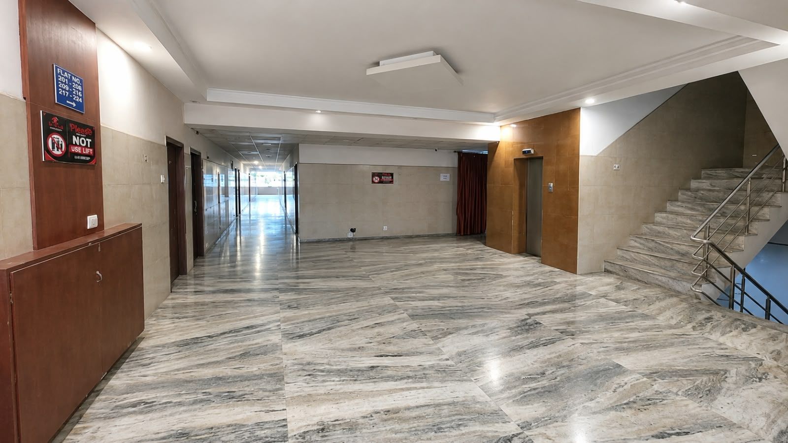 A spacious hallway with marble flooring, a staircase, and a sign indicating flat numbers.