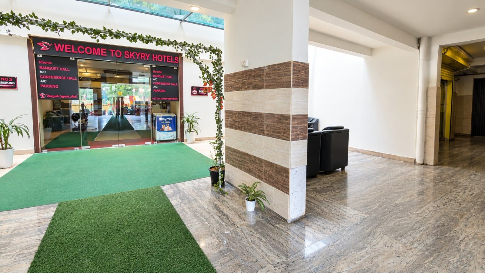 Zona de recepción de un hotel con alfombra verde, un mostrador de recepción y un cartel que enumera los servicios del hotel.