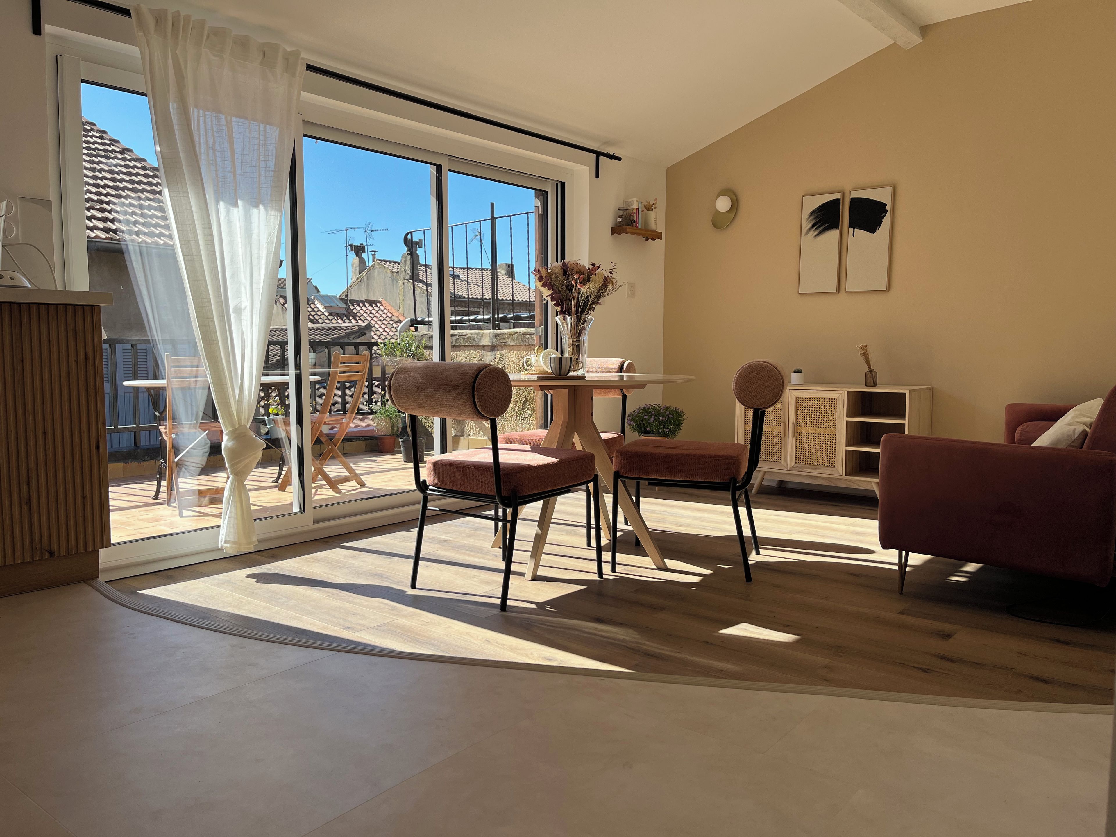 Een moderne woonkamer met een grote schuifpui die leidt naar een balkon, een eethoek met een tafel en stoelen, en een zithoek met een bank en fauteuils.