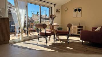 Een moderne woonkamer met een grote schuifpui die leidt naar een balkon, een eethoek met een tafel en stoelen, en een zithoek met een bank en fauteuils.