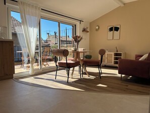 A modern living room with a large sliding glass door leading to a balcony, a dining area with a table and chairs, and a seating area with a sofa and armchairs. - (Avignon)