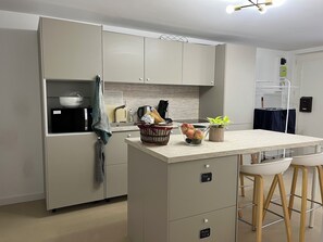 A modern kitchen with a central island, built-in cabinets, and a small seating area with stools. - (Avignon)
