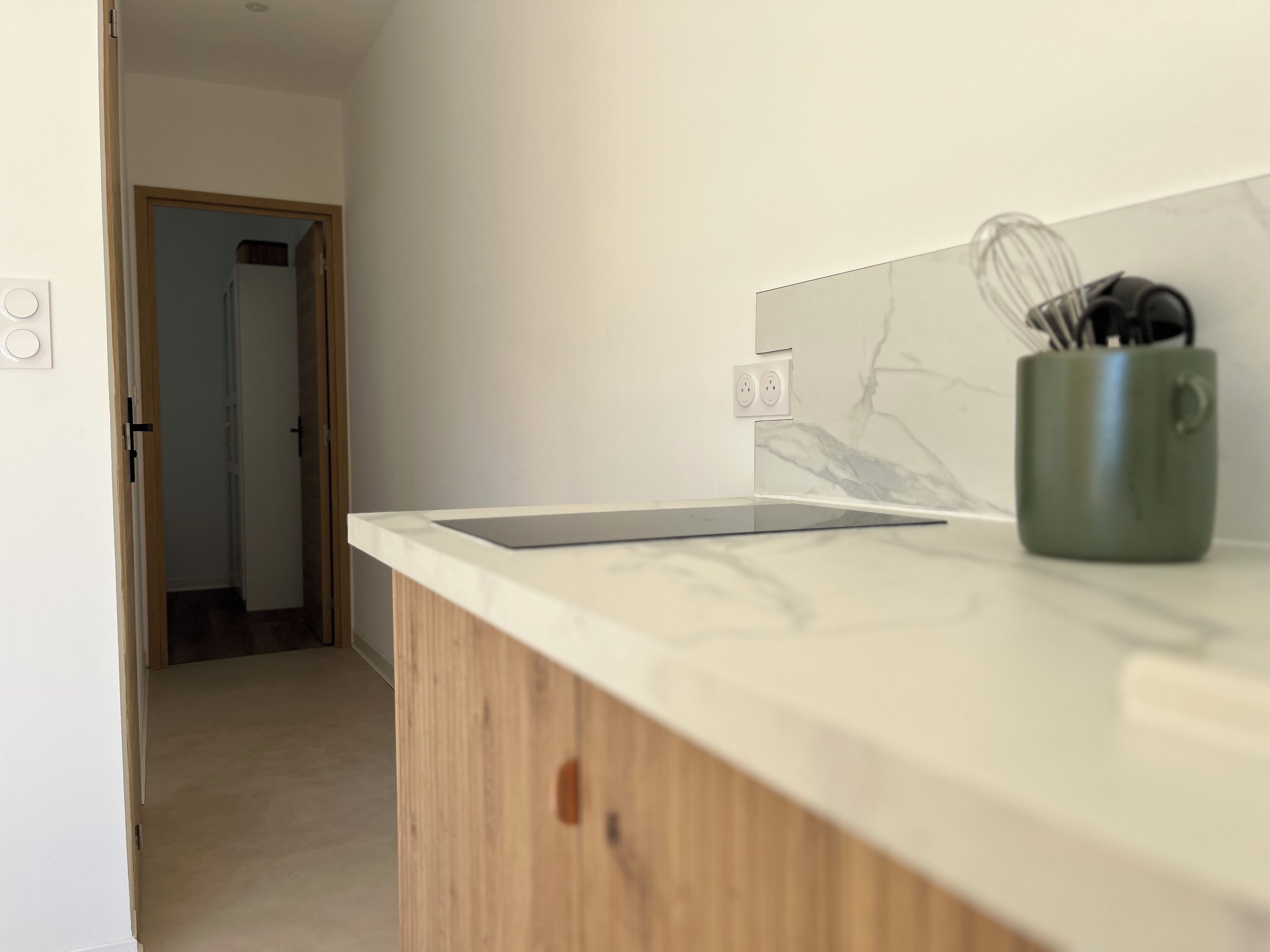 A kitchen with a marble backsplash, wooden cabinets, and a green mug with utensils.