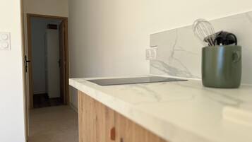 A kitchen with a marble backsplash, wooden cabinets, and a green mug with utensils.