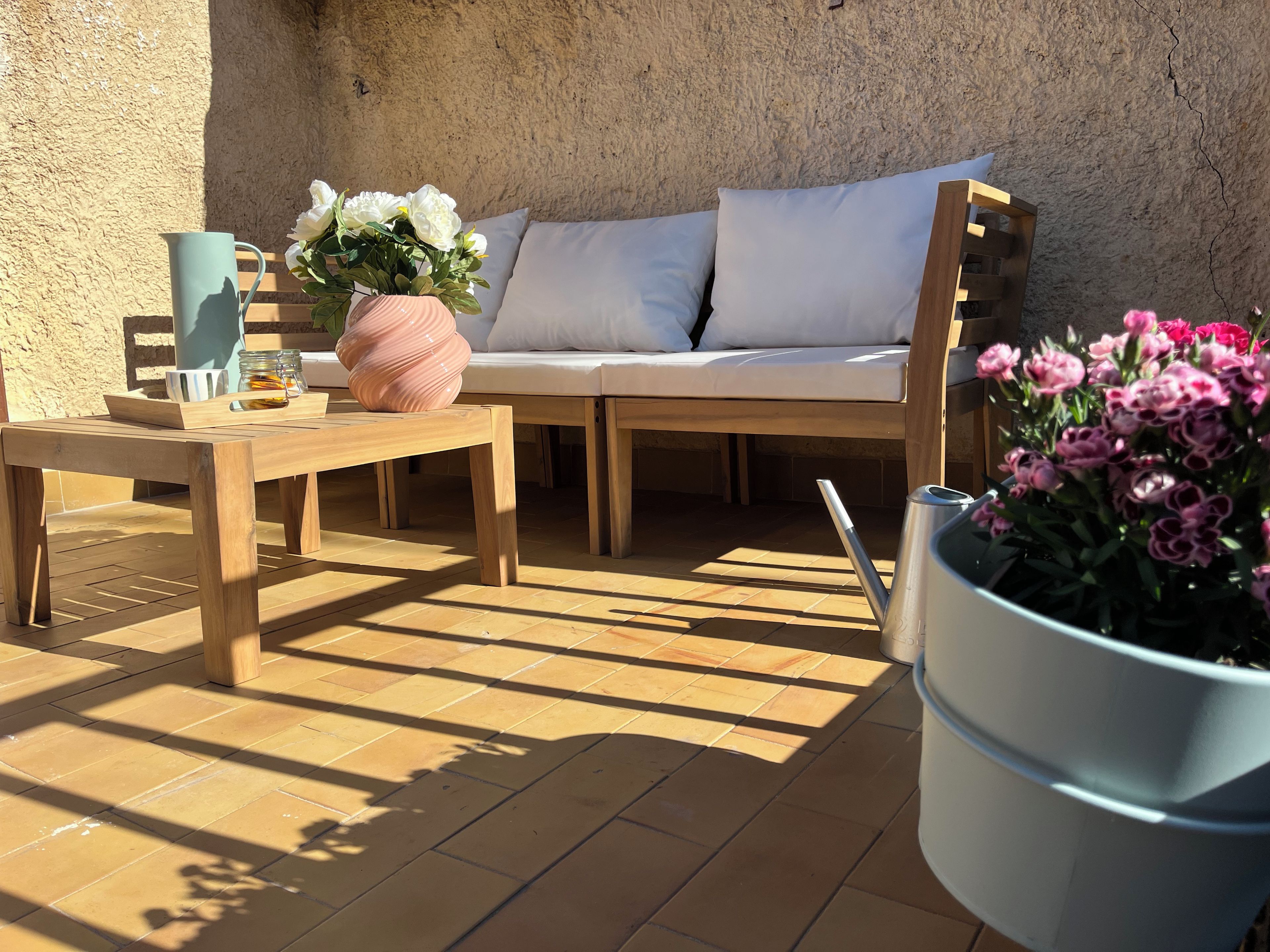A sunlit patio with a wooden table, a cushioned seating area, and a potted plant.