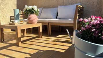 A sunlit patio with a wooden table, a cushioned seating area, and a potted plant.