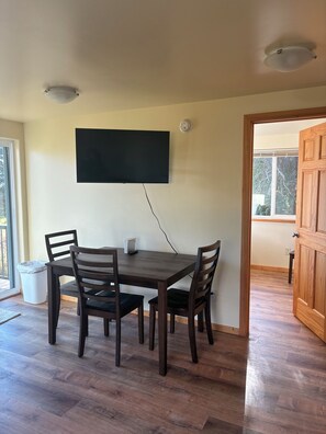 Un área de comedor con una mesa y sillas, un televisor de pantalla plana montado en la pared y una lámpara en el techo.