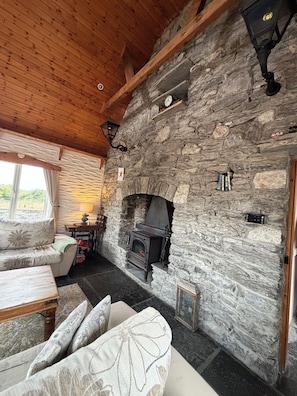 A stone fireplace with a modern stove, a wooden ceiling, and a sofa with floral cushions. - 3 bed 3 bath cottage; Minutes from Cliffs of Moher (CE)
