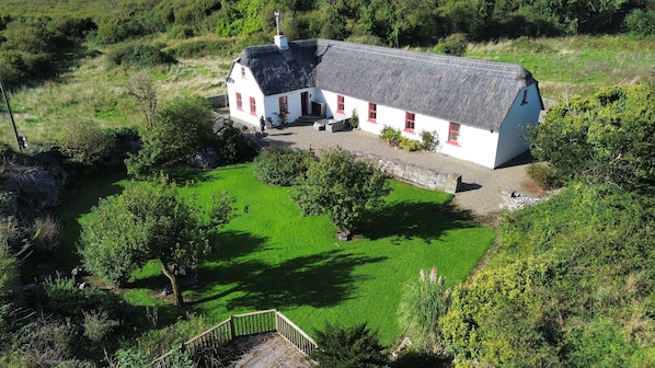 A white building with a grey roof, surrounded by a well-maintained lawn and trees. - 3 bed 3 bath cottage; Minutes from Cliffs of Moher (CE)