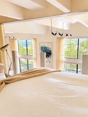Une chambre spacieuse avec un grand lit, de nombreuses fenêtres et un balcon.