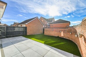 A residential backyard with a paved patio, a brick wall, and a grassy area. - 2-Bed Home with Parking Near Trent Bridge (Nottingham)