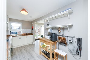Cozinha moderna com armários brancos, bancada de madeira e forno embutido. Há uma janela que oferece luz natural e vista para o exterior.