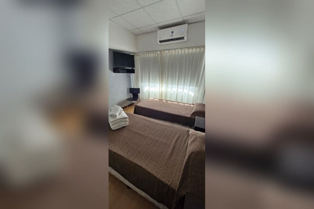 Quarto de hotel com duas camas, televisão de tela plana na parede, escrivaninha com cadeira e janela com cortinas.