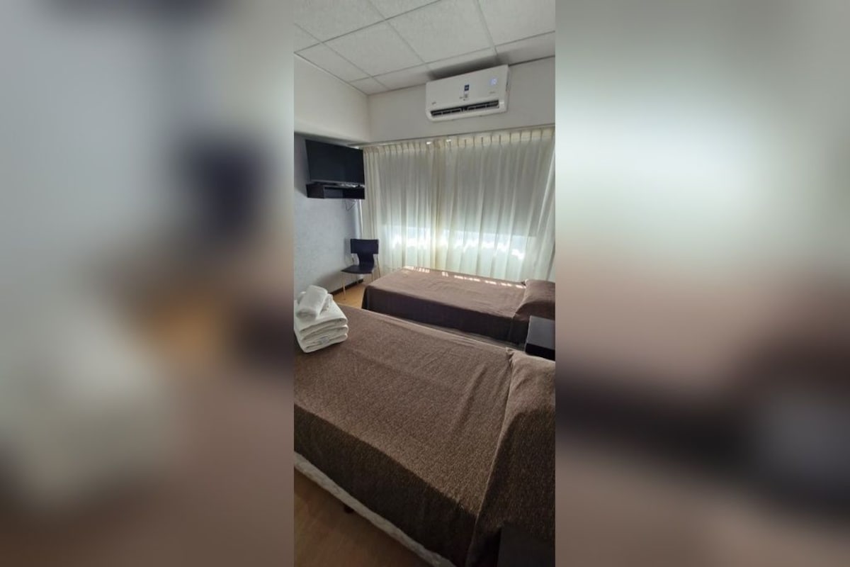 Ein Hotelzimmer mit zwei Betten, einem Flachbildfernseher an der Wand, einem Schreibtisch mit Stuhl und einem Fenster mit Vorhängen.