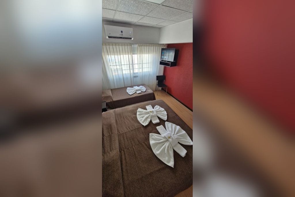 Une chambre d’hôtel avec deux lits, un téléviseur à écran plat fixé au mur et une fenêtre avec des rideaux.