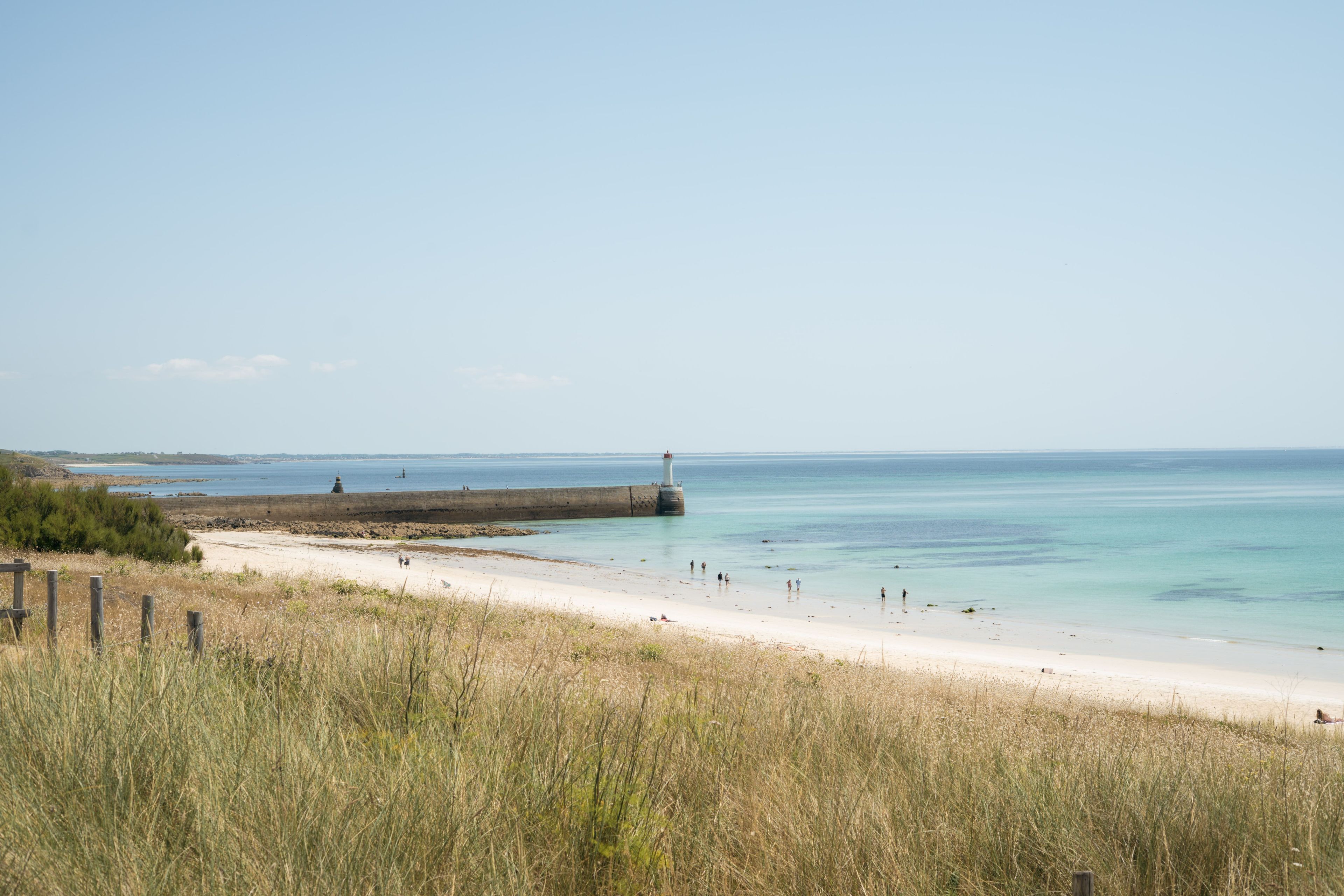 A coastal beach with a lighthouse, sandy shore, and grassy dunes.