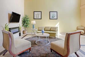 Ein Hotelzimmer mit einer Couch, zwei Sesseln, einem Couchtisch, einem Fernseher und gerahmten Pflanzenbildern an der Wand.