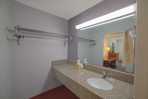 Un baño con encimera de granito, un lavabo blanco, un espejo y un perchero para toallas.