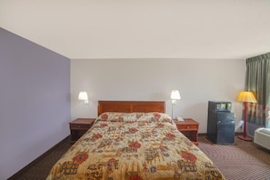 A hotel room with a bed, two bedside tables, a refrigerator, and a lamp.