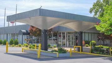 A modern building with a covered entrance, a glass facade, and a landscaped area with plants and a pathway.