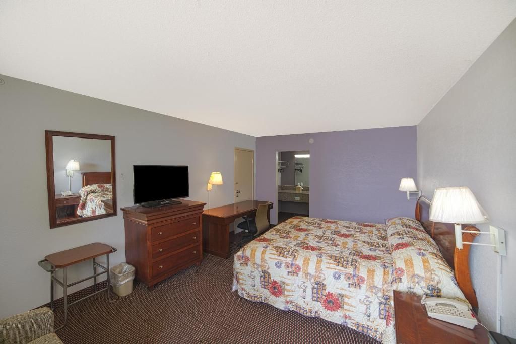 A hotel room with a bed, a dresser, a television, a desk, and a mirror.