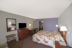 A hotel room with a bed, a dresser, a television, a desk, and a mirror.