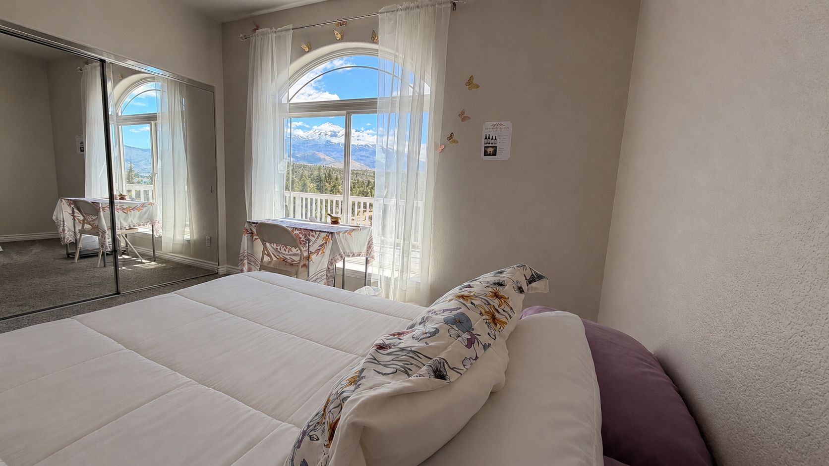 A hotel room with a large bed, a balcony with a table and chairs, and a view of mountains.