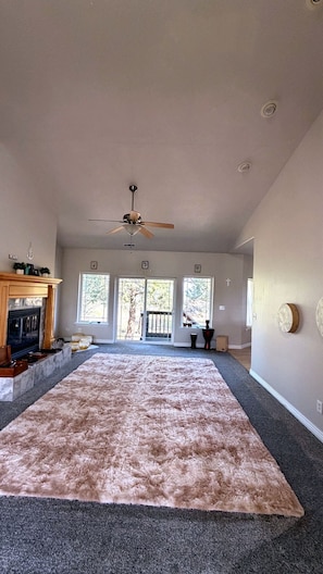 Un salon spacieux avec une grande moquette, une cheminée et un ventilateur de plafond.