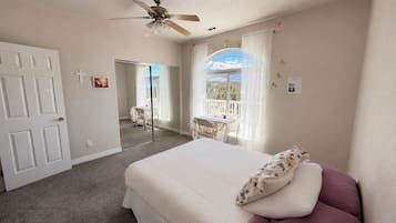 A bedroom with a bed, a ceiling fan, a window with curtains, and a balcony.