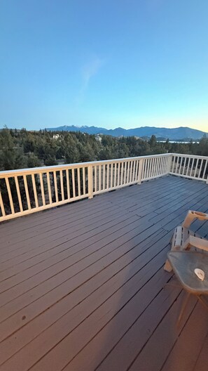 Een houten terras met een witte balustrade, met uitzicht op een bergachtig landschap.