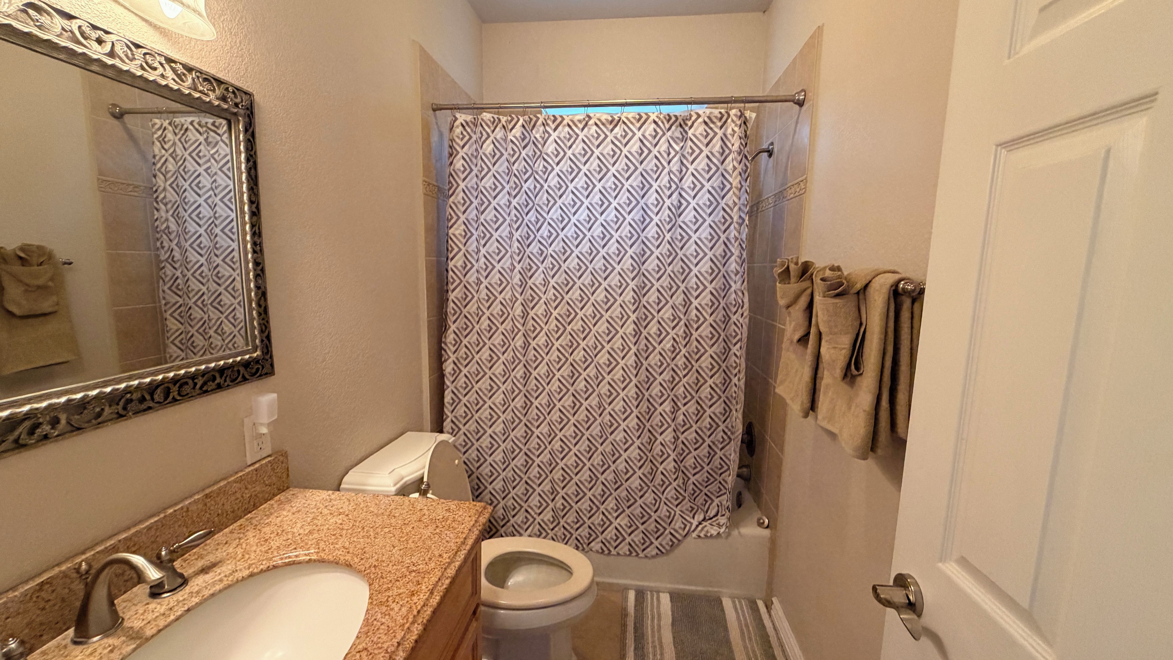 A bathroom with a toilet, sink, mirror, shower curtain, and towels on a rack.