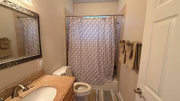 A bathroom with a toilet, sink, mirror, shower curtain, and towels on a rack.
