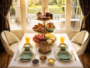 A breakfast setting with a tiered tray of pastries, fruits, and cheeses, a coffee and juice setup, and a view of a garden through a window. - Chateau Morreau (Péruwelz)