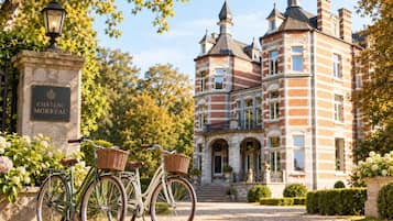 Un edificio histórico con un cartel que dice 'CHATEAU MORREAU', un camino pavimentado y una bicicleta con cestas.