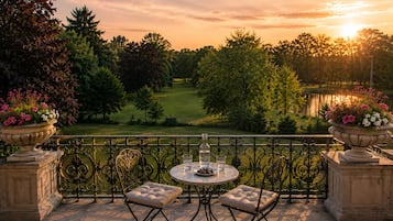 Un balcón con mesa y sillas, con vista a un campo de golf y una masa de agua al atardecer.