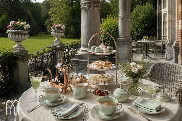 Une table dressée pour un service à thé en plein air, avec un présentoir à plusieurs niveaux où sont disposées des pâtisseries, des théières, des tasses et des soucoupes.