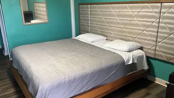 Una cama individual con estructura de madera y cabecera acolchada, ubicada frente a paredes color turquesa con un espejo arriba.